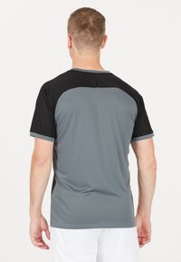 Grå och svart sportt-shirt med korta ärmar, med en slät och mjuk yta samt kontrasterande raglanärmar. Inga mönster eller detaljer.