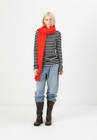 Červený vlnený šál s strapcami, čierno-biely pruhovaný dlhý rukáv, modré oversized džínsy a hnedé čižmy do výšky kolien.