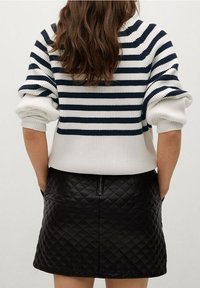 Pullover mit marineblauen und weißen horizontalen Streifen, gerippter Textur und hochgekrempelten Ärmeln, kombiniert mit einem schwarzen gesteppten Minirock mit einem rückseitigen Reißverschluss.