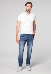 T-shirt bianco da uomo a maniche corte con scollatura a V abbinato a jeans in denim blu. I jeans presentano un design sbiadito e risvolti, abbinati a sneaker leggere.