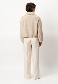 Fleece jack in lichtbeige met een zachte textuur en een kraag, gecombineerd met roomkleurige, gestructureerde, loszittende broek.