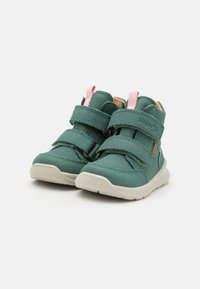 Zapatillas altas de imitación cuero verde con dos correas de Velcro, acentos rosas y una suela de goma con un patrón texturizado.