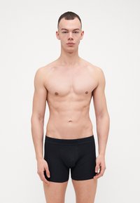 Svart bomullsboksershorts med bred elastisk midjebånd som har en subtil logo. Glatt tekstur og tettsittende design, vist på en nøytral bakgrunn.
