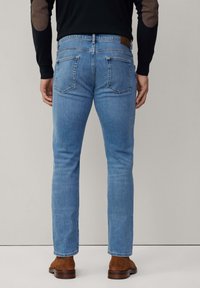 Vaqueros de mezclilla azul claro con corte ajustado, que presentan una etiqueta de cuero marrón en la cinturilla y dos bolsillos traseros. El usuario lleva botas marrones.