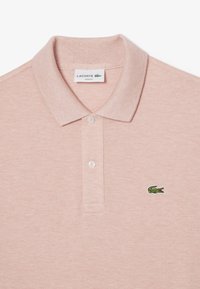 Ljusrosa polotröja i strukturerad tyg med slim fit. Har en klassisk krage, två knappar och en grön broderad logotyp.