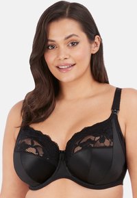 Sottobusto nero con ferretto, caratterizzato da dettagli in pizzo floreale nella parte superiore e sezioni in rete. Coppe in nylon lisce con spalline regolabili e chiusura a gancio.