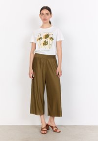 White t-shirt with floral graphic in green and gold, paired with olive green pleated wide-leg pants. Brown heeled sandals complete the outfit.