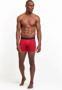 Boxers rouges avec une ceinture élastique noire portant le nom de la marque "FALKE" en lettres rouges. Texture lisse et coupe ajustée.
