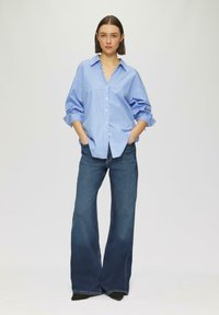 Blauw-witte gestreepte overhemd met knopen, met een losse fit, gedragen met donkerblauwe wijde jeans en zwarte hakken; zachte textuur.