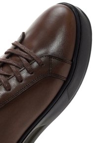 Zapato de cuero marrón con una textura suave, puntera redonda y suela de goma oscura con un agarre estampado. Los cordones son marrones y trenzados.