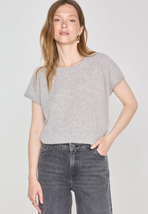 Maglione grigio chiaro a maniche corte realizzato in tessuto morbido, con scollatura rotonda e vestibilità rilassata, abbinato a jeans a vita alta grigio scuro.