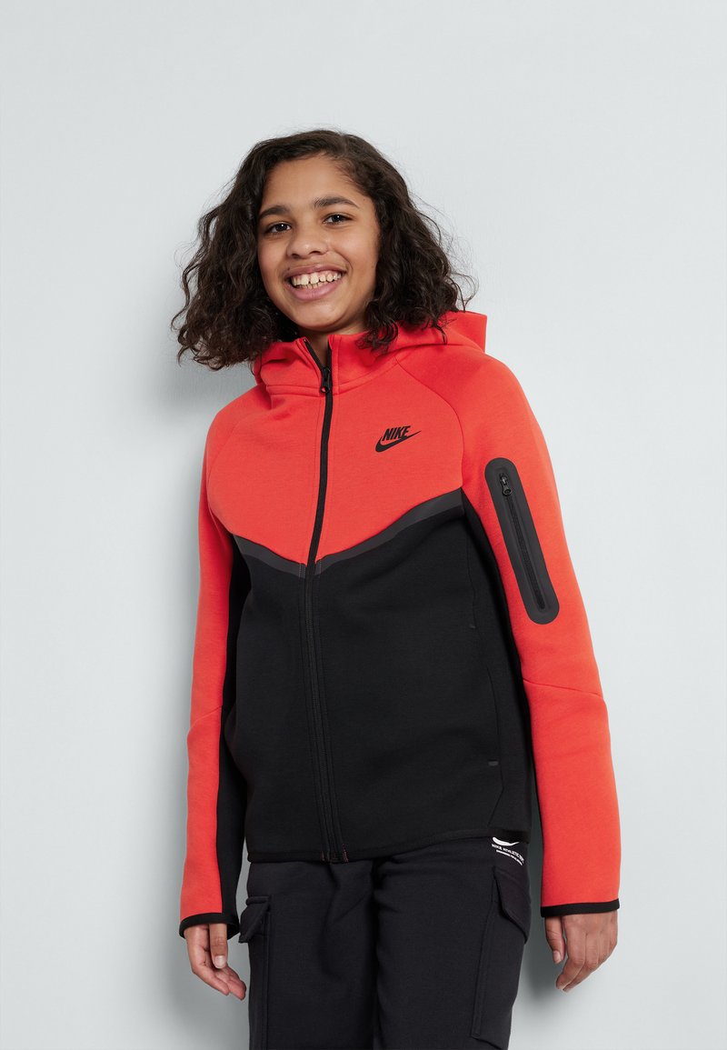 Nike zip-up hette i klar orange og svart, med et kontrasterende øverste design, glidelås-lomme på siden og teksturert materiale.