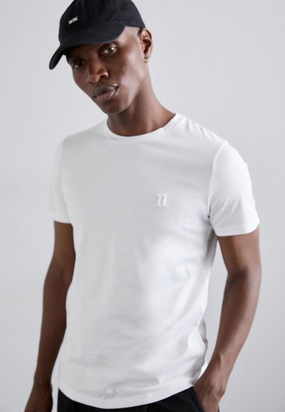 T-shirt blanche à manches courtes avec un col rond et un logo texturé subtil, associée à une casquette de baseball noire ornée d'un petit design blanc.