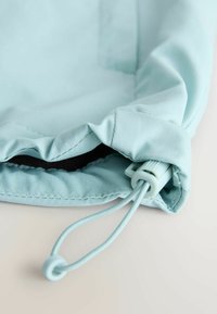 Lichtblauw stoffen tasje met een trekkoord en een plastic grendel, licht geopend op een witte ondergrond.