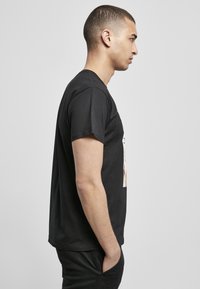 Black cotton t-shirt with a crew neck, short sleeves, featuring a printed graphic on the front. Tapered fit, smooth texture.