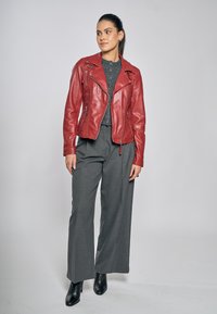 Rode leren motorjack met asymmetrische rits, revers en ritssluitingen. Gecombineerd met grijze, brede broekspijpen en zwarte enkellaarzen.