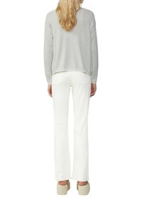 Un pull gris à manches courtes sur un jean flare blanc, avec une coupe décontractée et une texture légère. Des chaussures à plateforme ajoutent de la hauteur et une couleur neutre.