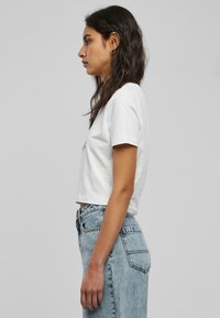 Hvit cropped t-skjorte med rund hals, korte ermer og subtil grafisk detalj på forsiden. Kombinert med høyhælte lyseblå jeans.