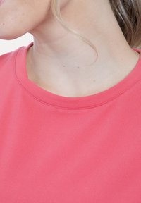 Maglietta di cotone rosa corallo con scollo tondo e texture liscia, che mostra una vista ravvicinata del tessuto e del dettaglio del colletto.