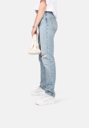 Light blue denim jeans with a relaxed fit, featuring distressed knee rips, paired with white sneakers and a cream handbag.
