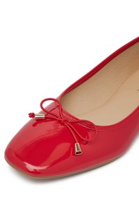 Červené lakované baleríny s špicatou špičkou, obsahujúce ozdobnú mašľu a zlaté kovové detaily. Hladká textura a jednoduchý dizajn.