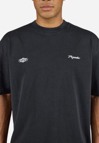Sort bomulds T-shirt med rund halsudskæring. Har hvid tekst på forsiden: "Pegador" og et lille mærke der siger "Hvor drømme er lavet af."