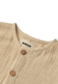 Beige linnesskjorta med rund halsringning, prydd med två träknappar och en texturerad, något skrynklig yta. Etiketten säger "WHEAT."