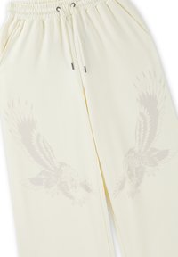 Cream-colored pants with elastic waistband and drawstring, featuring subtle printed eagle designs on each leg.
