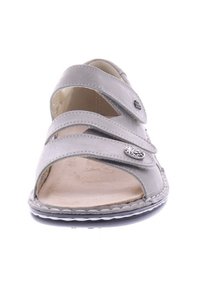 Hellgraue Sandale mit zwei verstellbaren Riemen, einer genähten Kante und einer strukturierten Innensohle. Dekorativer Metallakzent in der Nähe des Riemens.