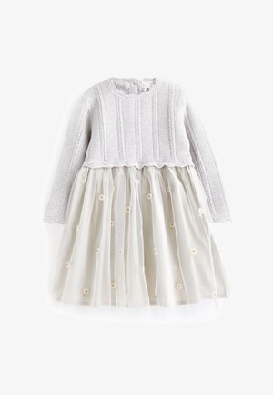 Top de punto gris con mangas largas y cuello redondo, combinado con una falda transparente color crema con bordado floral. Detalle de dobladillo con forma de ondas.