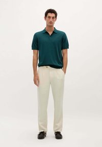 Teal polo med krave, parret med lysebeige linnedragter og mørke sko. Sættet har en afslappet pasform og glatte teksturer.