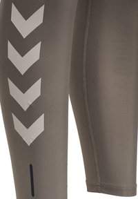 Nærbillede af grå sportsleggings med hvide nedadvendte chevronstriber og synlige syninger.