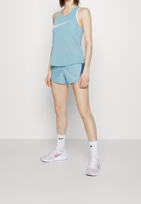Ljust blå Nike tanktopp, matchande shorts och ljusrosa sneakers med vita och svarta accenter. Slät tyg med sportig passform.