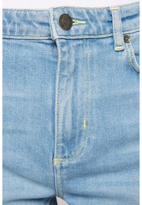 Jeans de mezclilla de color azul claro con cremallera y cierre de botón, con acentos de costura amarilla y un diseño clásico de cinco bolsillos.