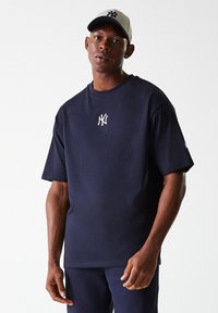 Marineblå bomull T-skjorte med korte ermer, rund hals, og en hvit logo på brystet. Kombinert med en beige caps med en mørk logo.