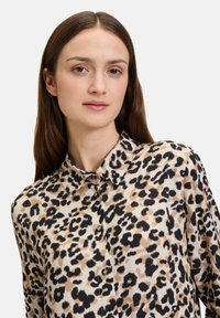 Leopardenmuster-Bluse aus leichtem Stoff, mit Kragen, Knopfleiste und unterschiedlichen Beigetönen und schwarzen Mustern.