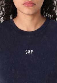 Marineblå ribbet sweatshirt med et hvidt broderet "GAP" logo på brystet. Rund krave, tekstureret stof og tætsiddende design.