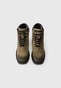 Botas de pele castanha com detalhes em preto, apresentando atacadores robustos, colarinho almofadado e solas texturizadas para melhor aderência. Design de bico arredondado.