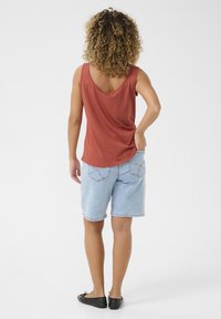 Röd ärmlös topp med rundad rygg; ljusbl�å denimshorts med fransade kanter och bakfickor; svarta platta skor.