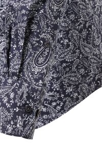 Manica di camicia blu marino con motivo paisley e floreale bianco, caratterizzata da due bottoni neri sul polsino.