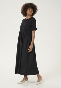 Juoda, iki kelių siekianti suknelė su trumpomis rankovėmis ir susiraukusiu sijonu. Lygi medvilnės tekstūra, paprastas apvalus kaklas ir minimalistinis dizainas.