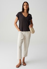 T-shirt nera a scollo a V con maniche corte, abbinata a pantaloni beige a gamba larga e infradito. Il modello tiene una borsa intrecciata beige.