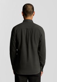 Camisa de manga larga verde oscuro hecha de tela texturizada, con un collar en punta, puños abotonados y un dobladillo recto.