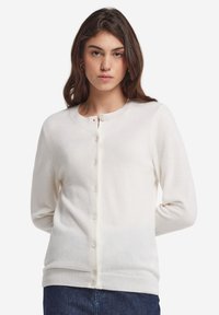 Vit stickad kofta med rund halsringning, långa ärmar och knäppning. Mjuk textur och ribbat nederkant.