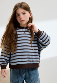 Sudadera a rayas azules y marrones con cuello redondo y ajuste holgado, combinada con pantalones vaqueros de cintura alta. Textura suave, diseño casual.