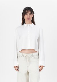 White cropped button-up shirt with a collar and long sleeves. Smooth texture, featuring a straight hem and subtle button detailing.