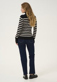 Prugasta crno-bež rolka s dugim rukavima i bočnim prorezima, uparena s tamnoplavim trapericama i crnim cipelama.