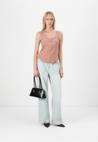 Lichtroze geribbelde tanktop met knopen, gecombineerd met lichtblauwe wijde jeans. Geaccessoiresd met een zwarte handtas en puntige zwarte flatjes.