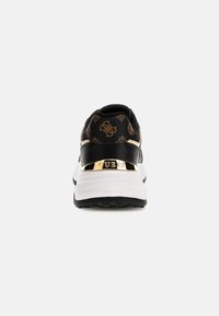 Baskets de créateur noires et brunes avec motif monogramme, semelle épaisse blanche et accent doré portant le nom de la marque au talon.