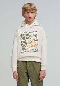 Felpa con cappuccio in bianco sporco, con grafica sul fronte che presenta un teschio e testo in verde e arancione. Polsini e orlo a coste. Vestibilità casual.